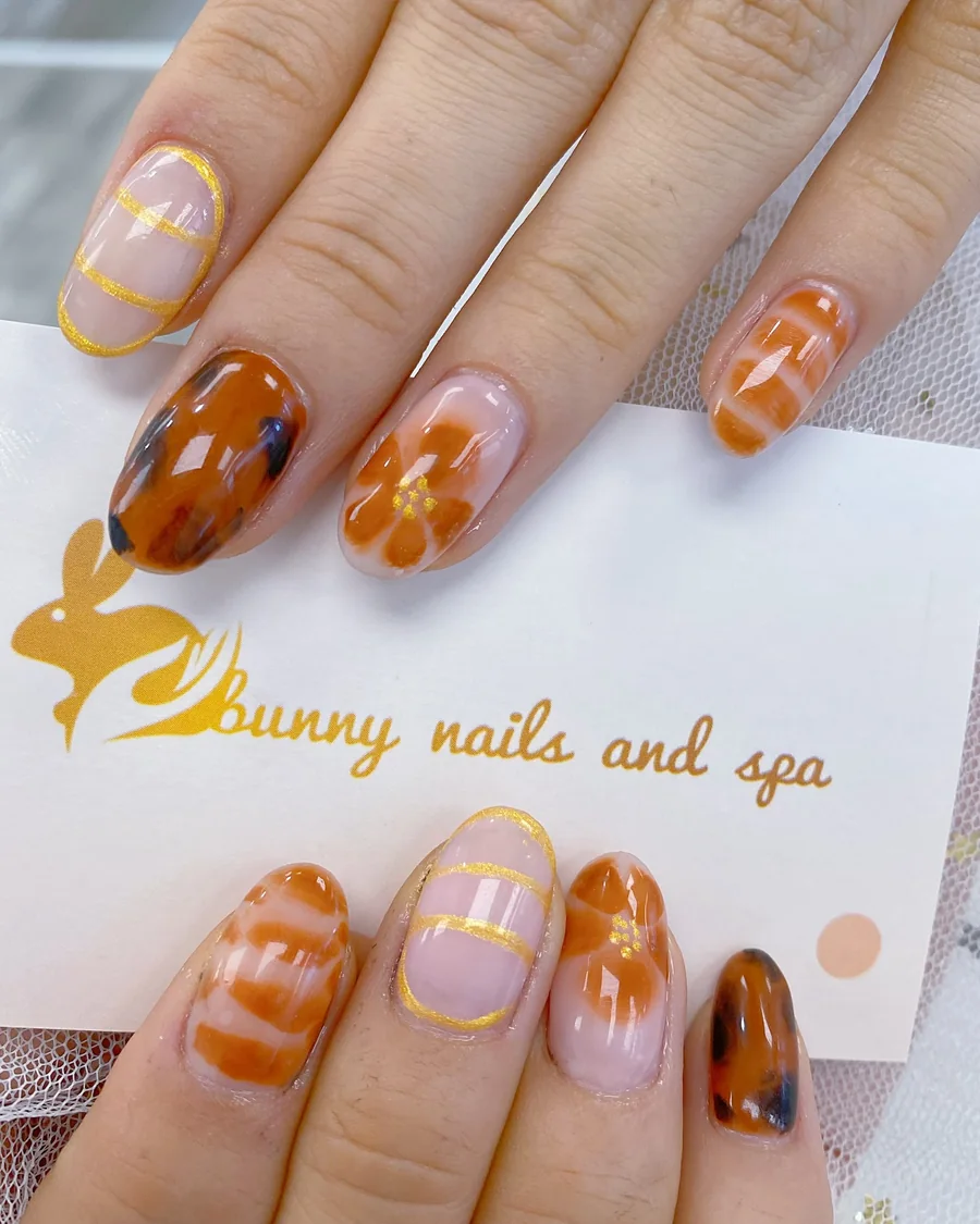 Oval nails in burnt orange stripes, tortoiseshell and gold line work, done at Bunny Nails & Spa