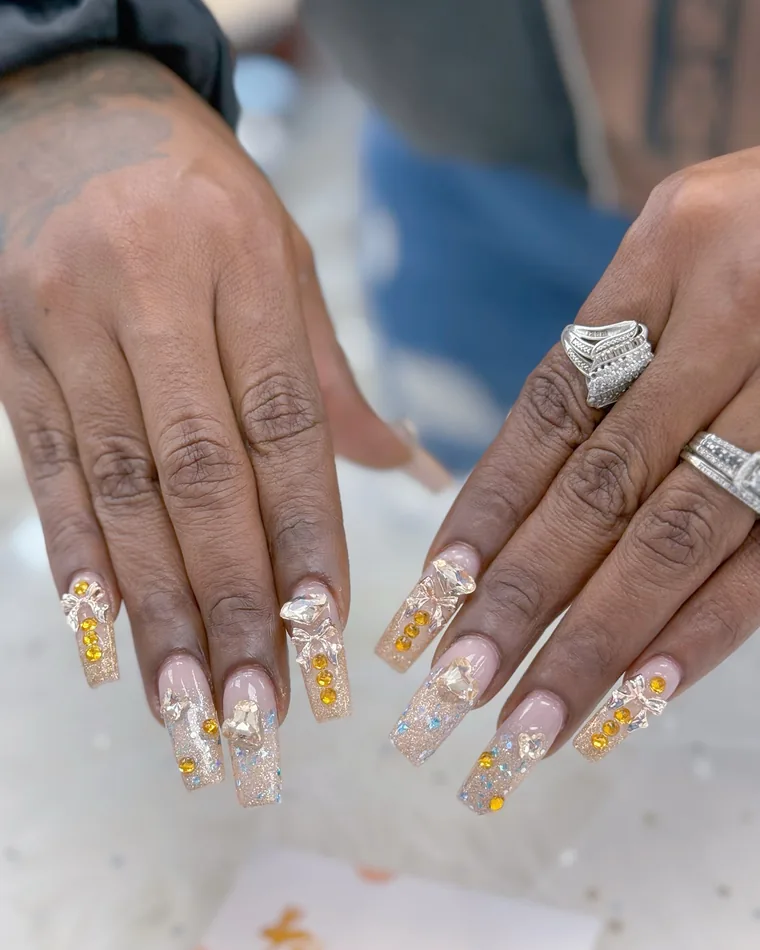 Long coffin nails in champagne glitter with 3D bows and amber rhinestones