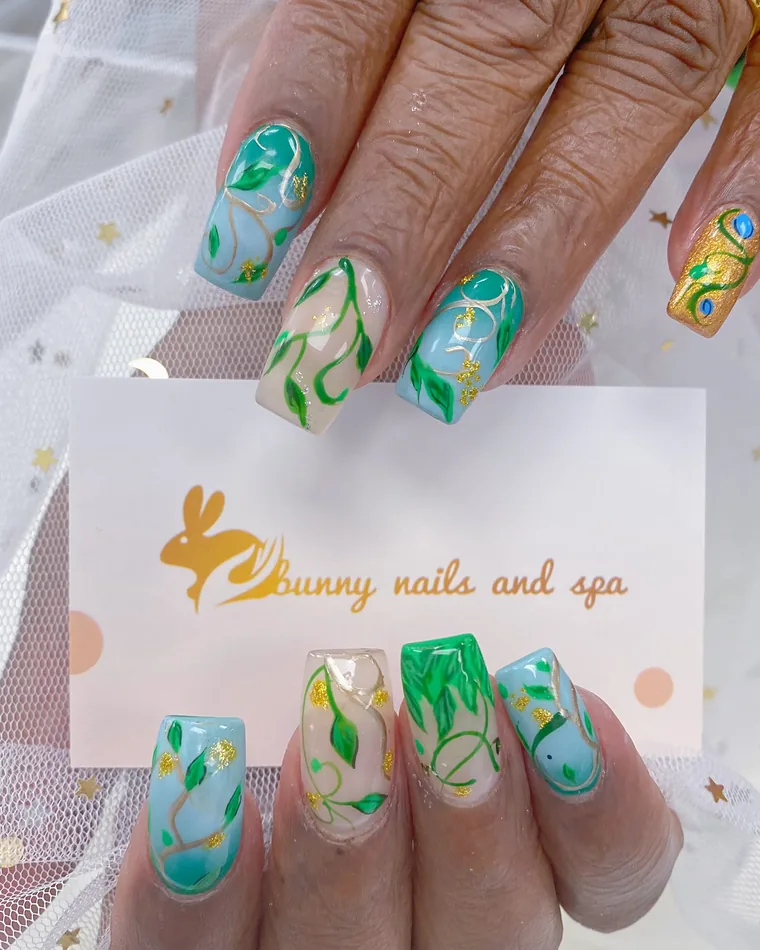 Square nails painted with green vines, leaves and gold glitter