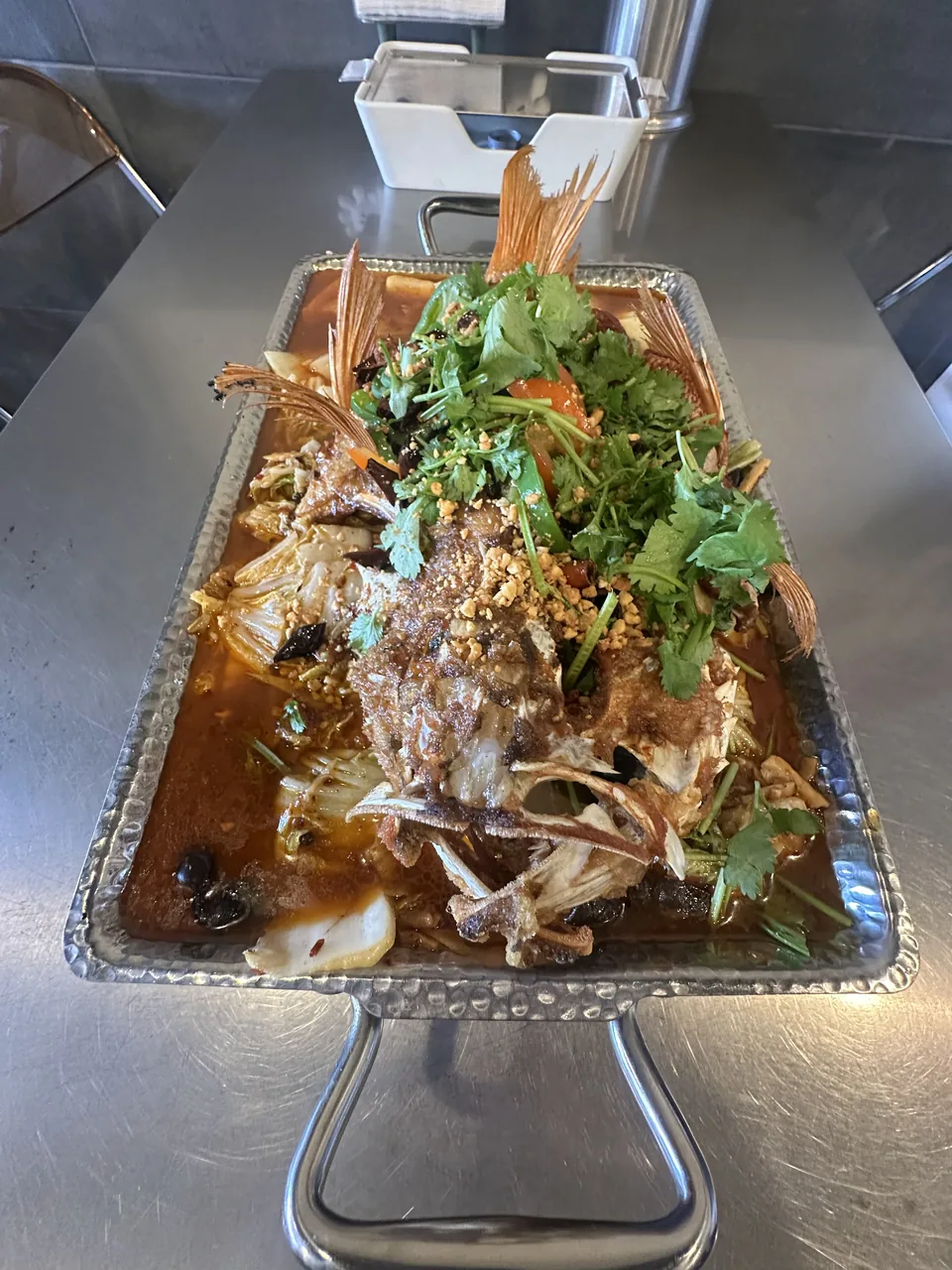 A whole grilled fish topped with cilantro in a foil tray