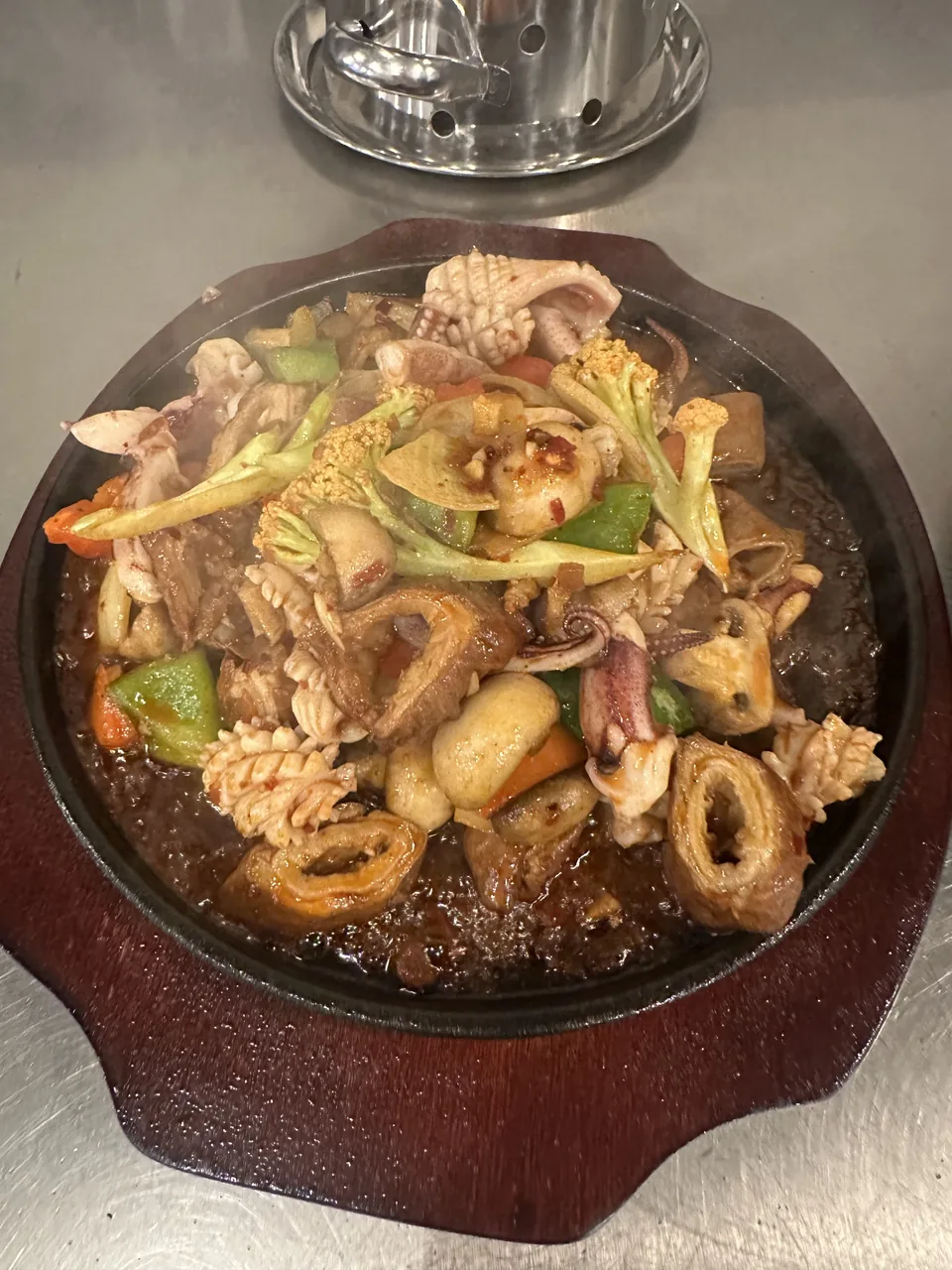 A sizzling hot plate of squid, peppers and onion on a cast-iron platter