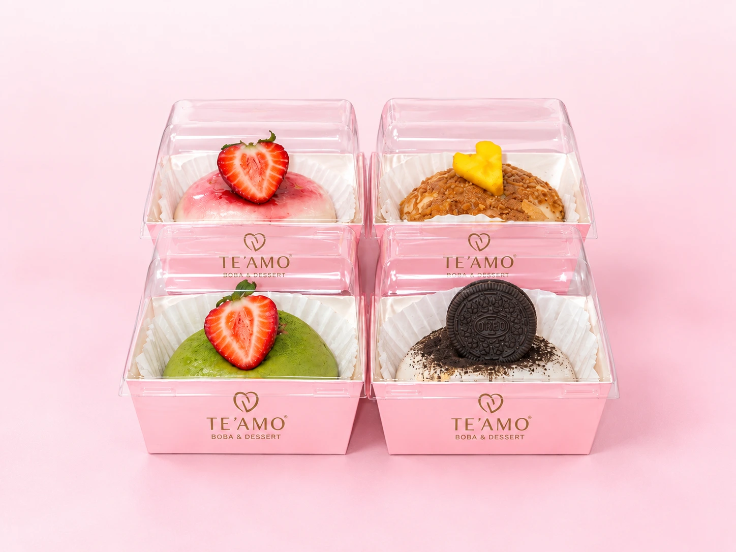 Four TE’AMO handmade cheesecake mochi in pink boxes on a blush pink background: strawberry, mango, matcha strawberry and Oreo
